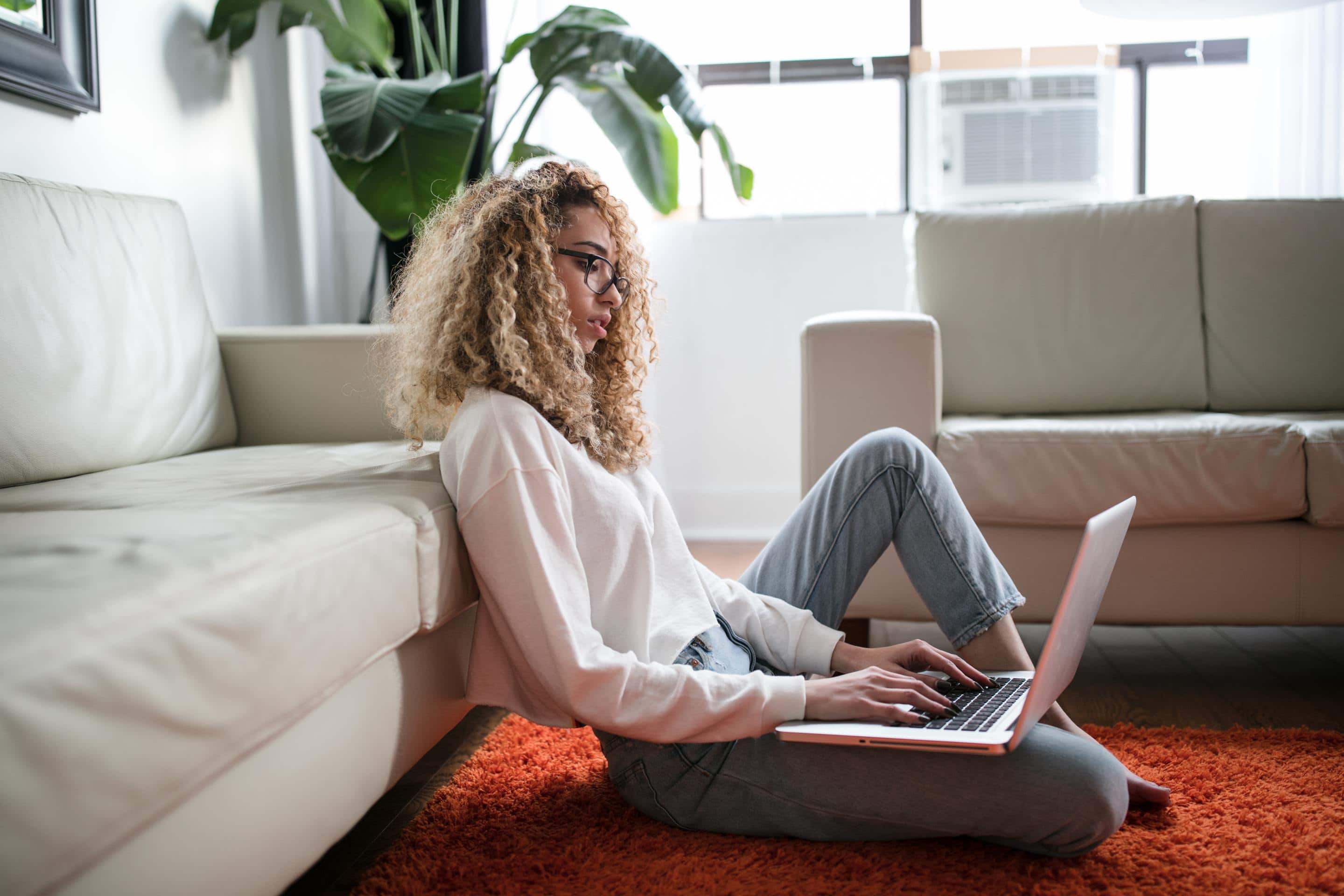 Woman on floor looking thoughtfully at laptop